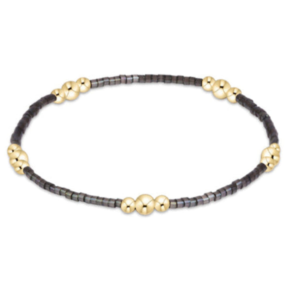 A delicate beaded bracelet featuring a dark gray beaded base with small gold-toned decorative beads spaced along the front, displayed on a clean white background.