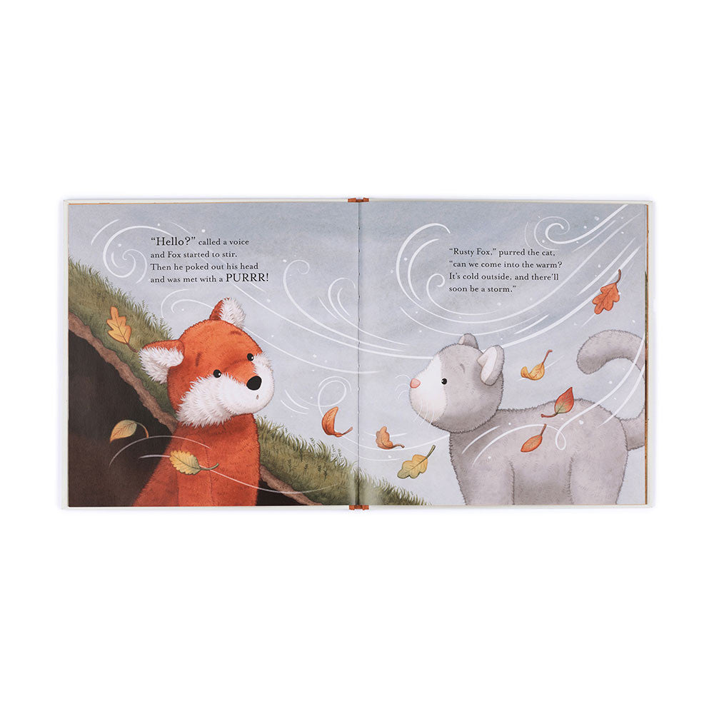 The opened book 'Warm in the Storm' with a fox and cat with black text, grass and leaves being blown in the wind.