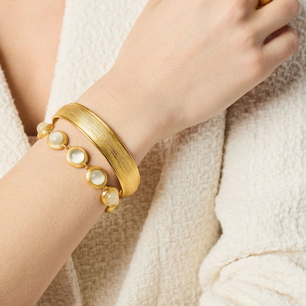 Gold bracelet with pearl-like stones on a wrist against a neutral background
