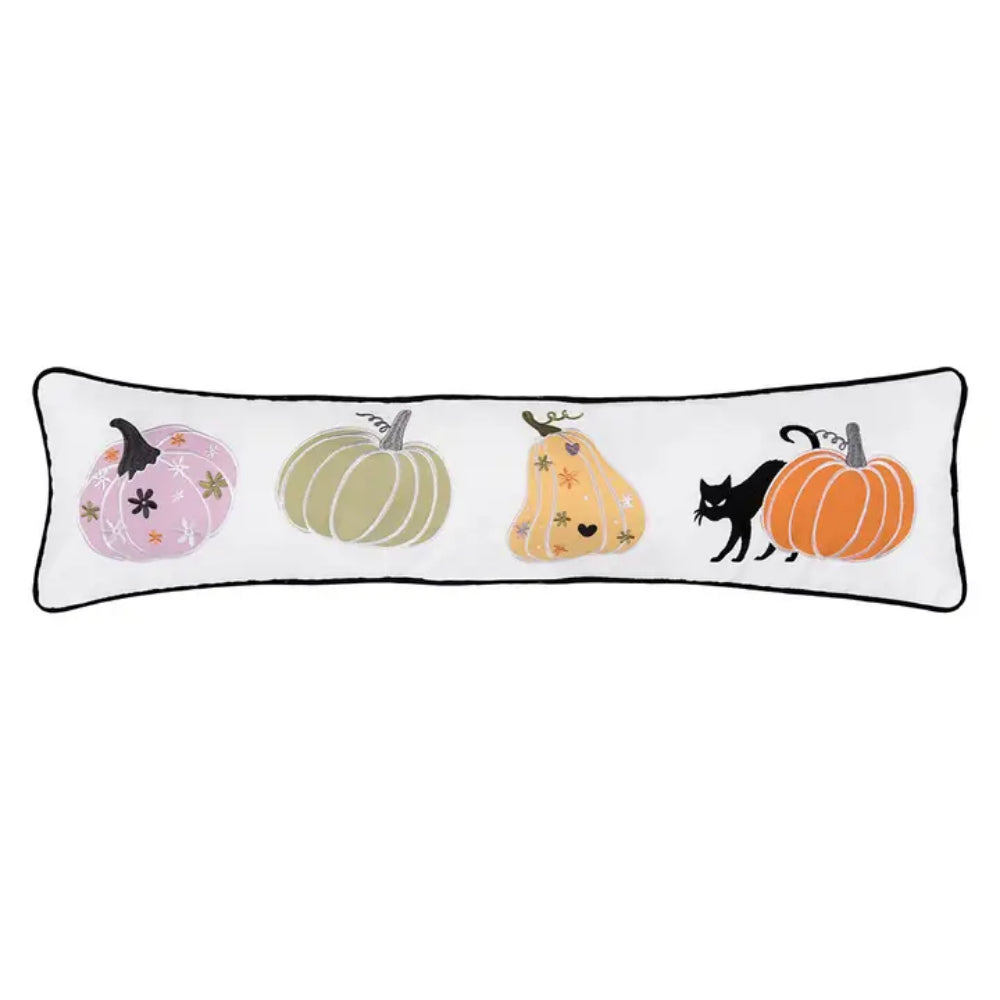 A long rectangular white throw pillow with a black piped border, featuring a row of stylized pumpkins and black cats in pastel and bright colors.