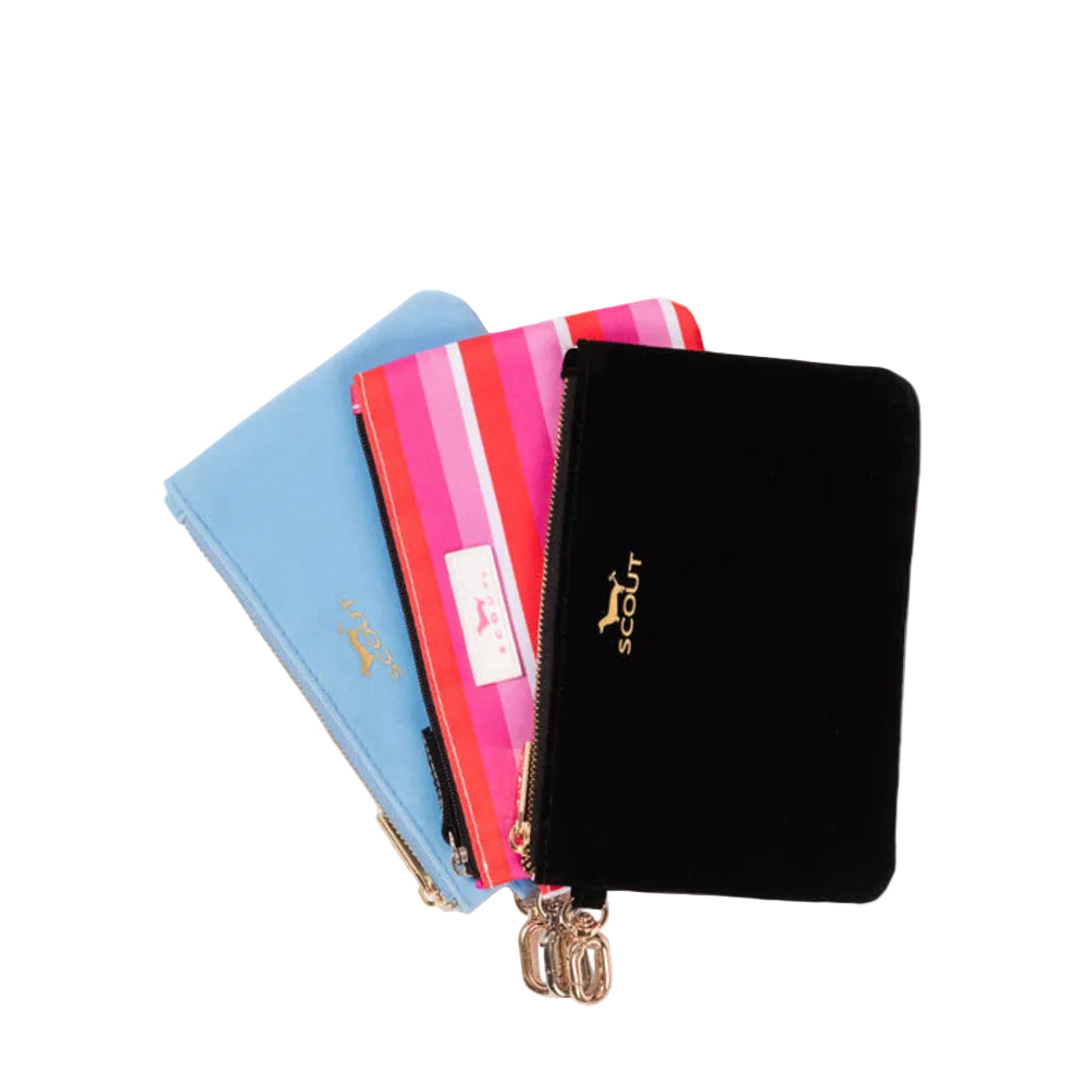 Three Scout zippered pouches stacked on a white background: a light blue one, a pink and orange striped one, and a black velvet one with gold logo.
