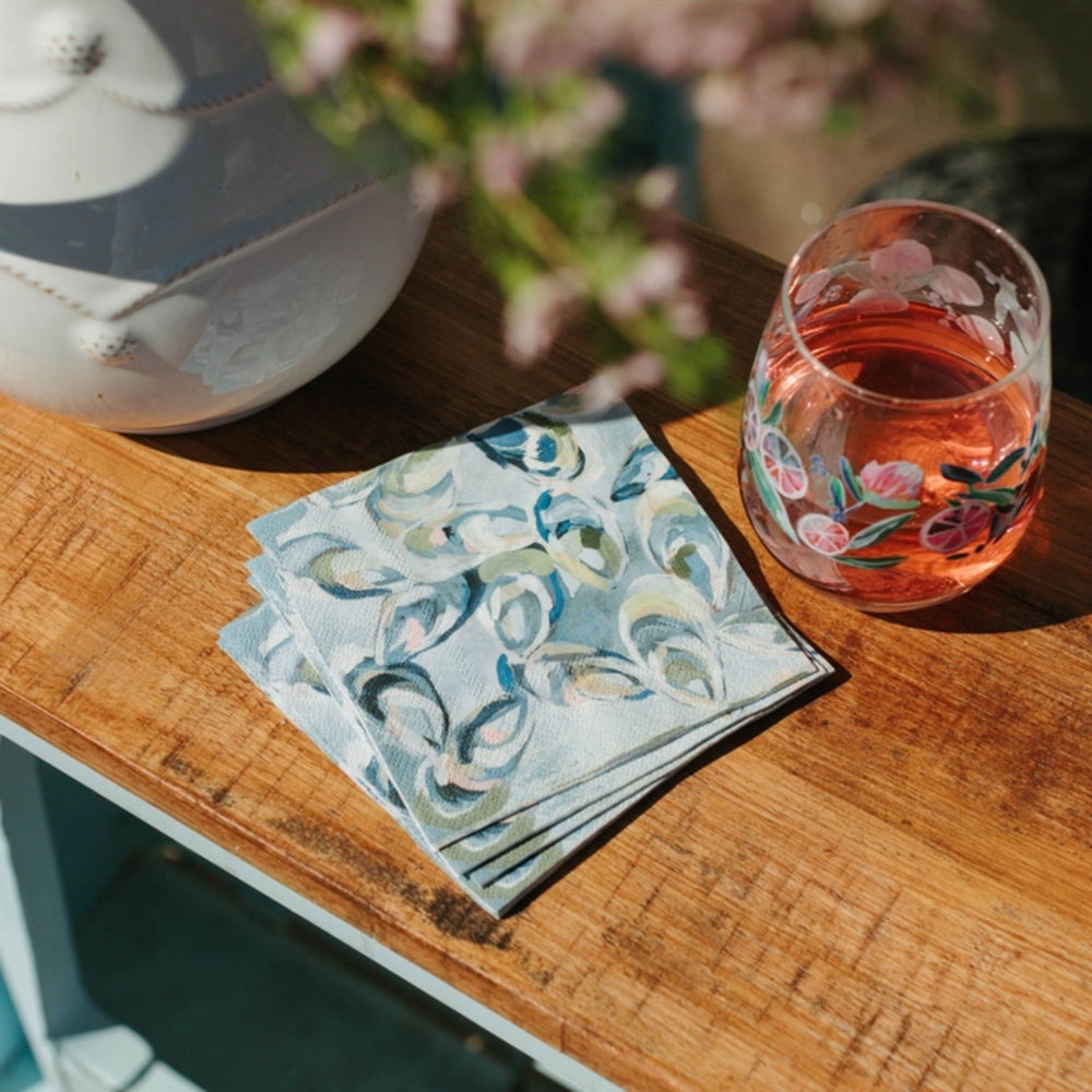Stack of patterned napkins on a wooden surface with a glass of pink drink in the background.