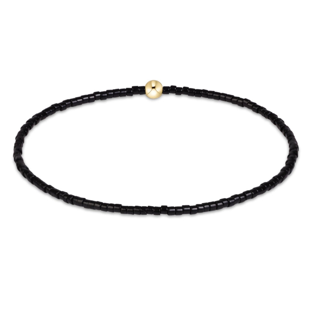 A delicate black beaded bracelet with a single polished gold bead accent at the top, displayed on a clean white background.