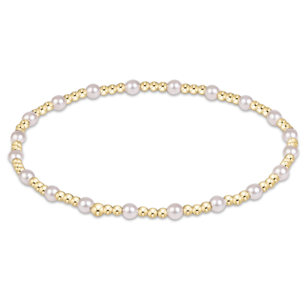 A delicate beaded bracelet featuring small white pearls and gold-toned beads, arranged in a horizontal oval on a solid white background.