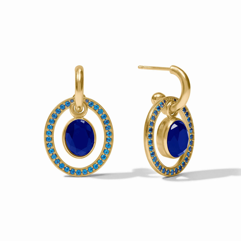 A pair of gold hoop earrings with oval blue cabochon centers and a halo of small bright blue stones, shown on a clean white background.
