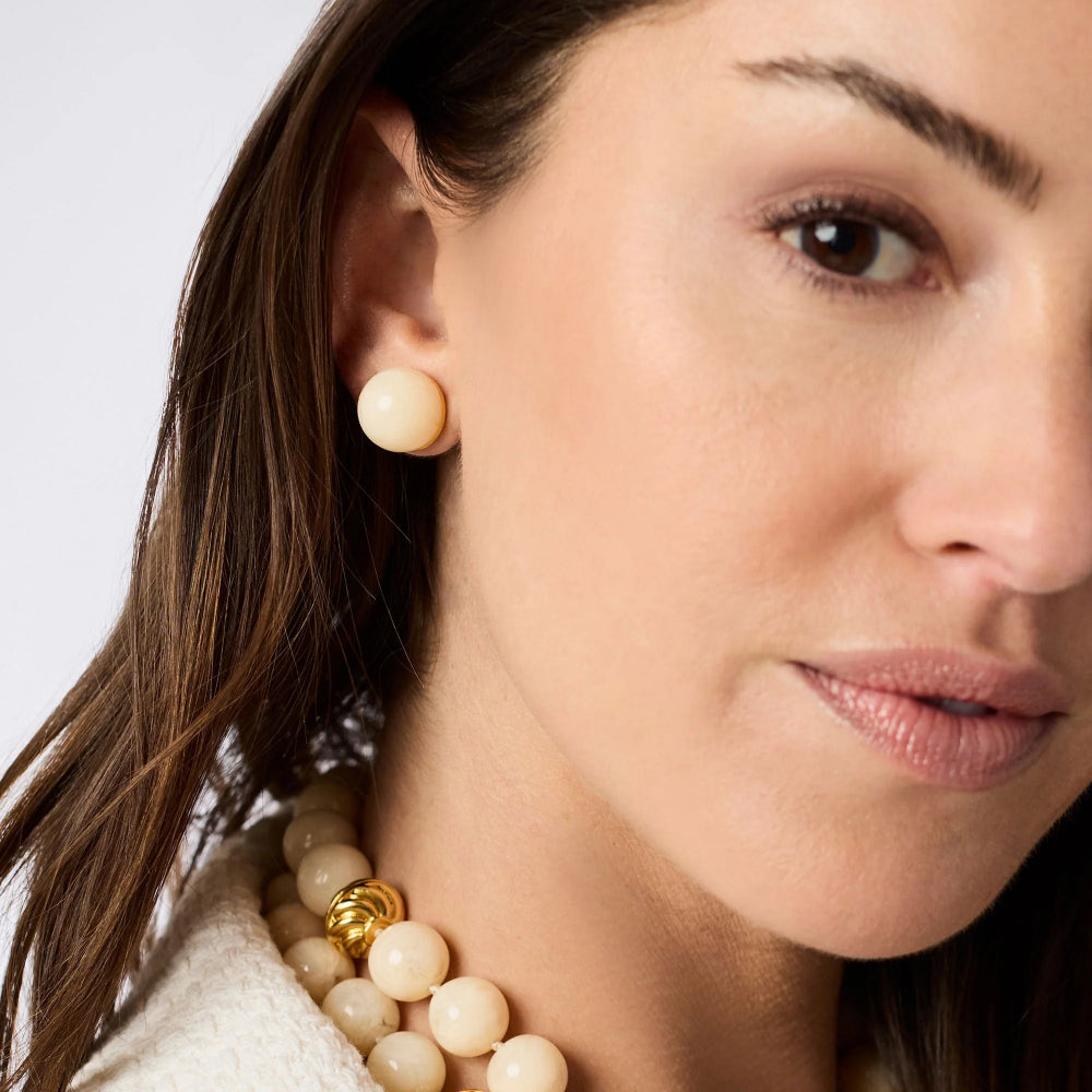 Close-up of a woman wearing pearl earrings and a necklace against a light background