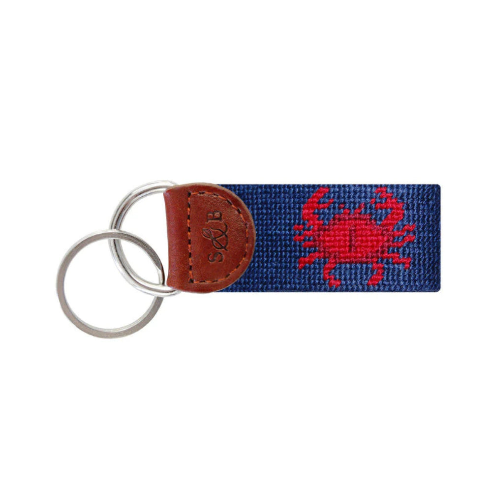 A navy blue woven canvas keychain with a red embroidered crab motif and a brown leather tab featuring an embossed 'S&B' logo, attached to two silver metal key rings.