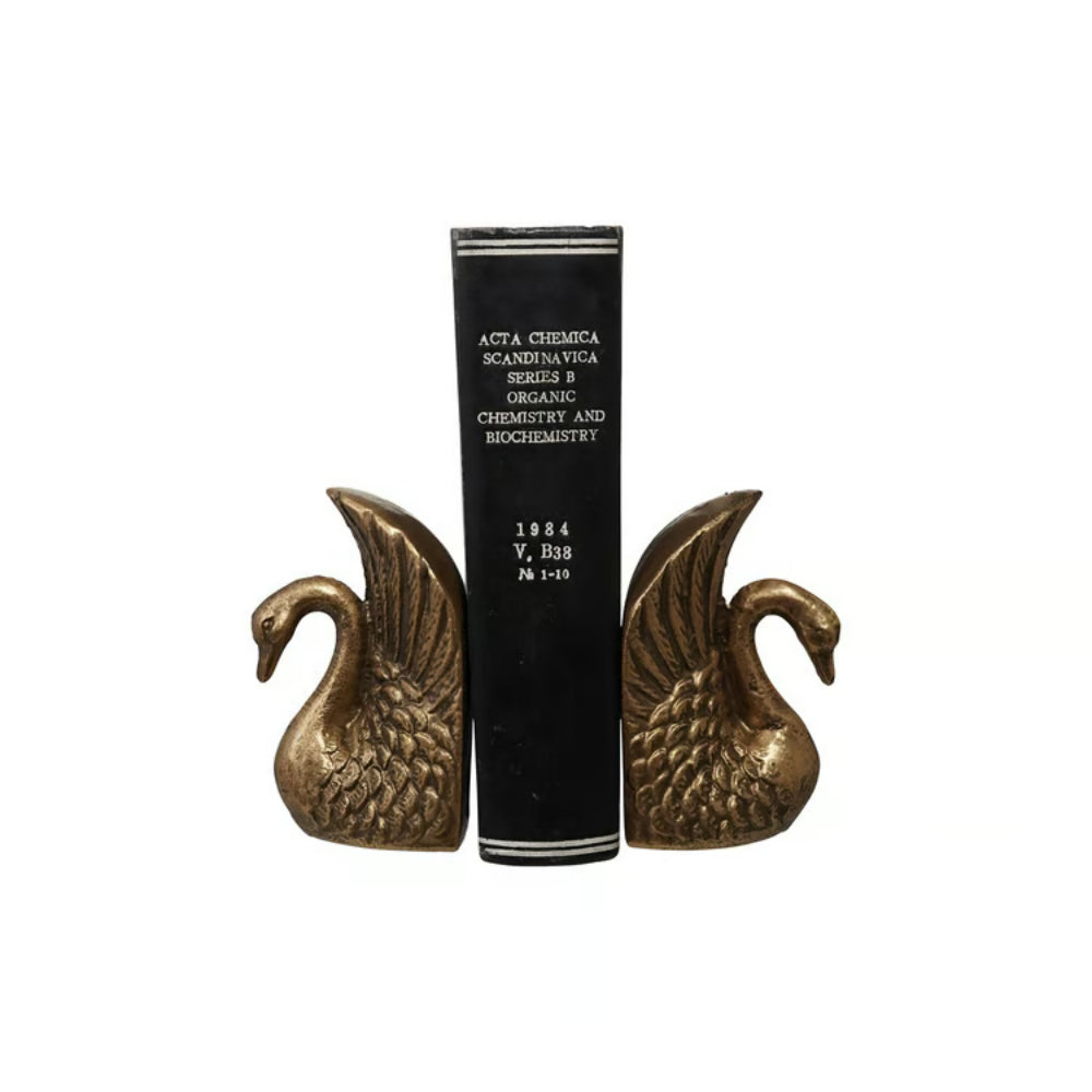 A pair of antique-style bronze swan bookends holding a black hardcover book upright against a plain white background.