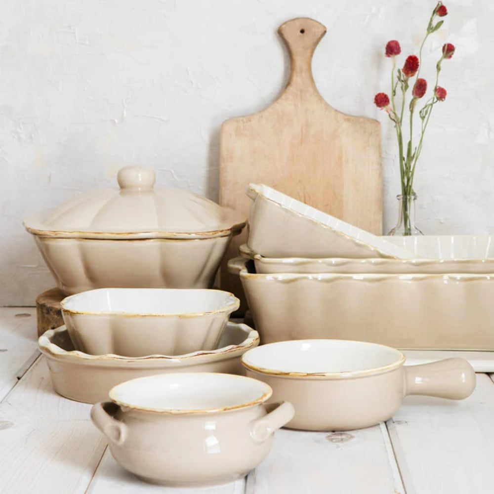 Set of beige ceramic cookware with gold trim on a white wooden surface.