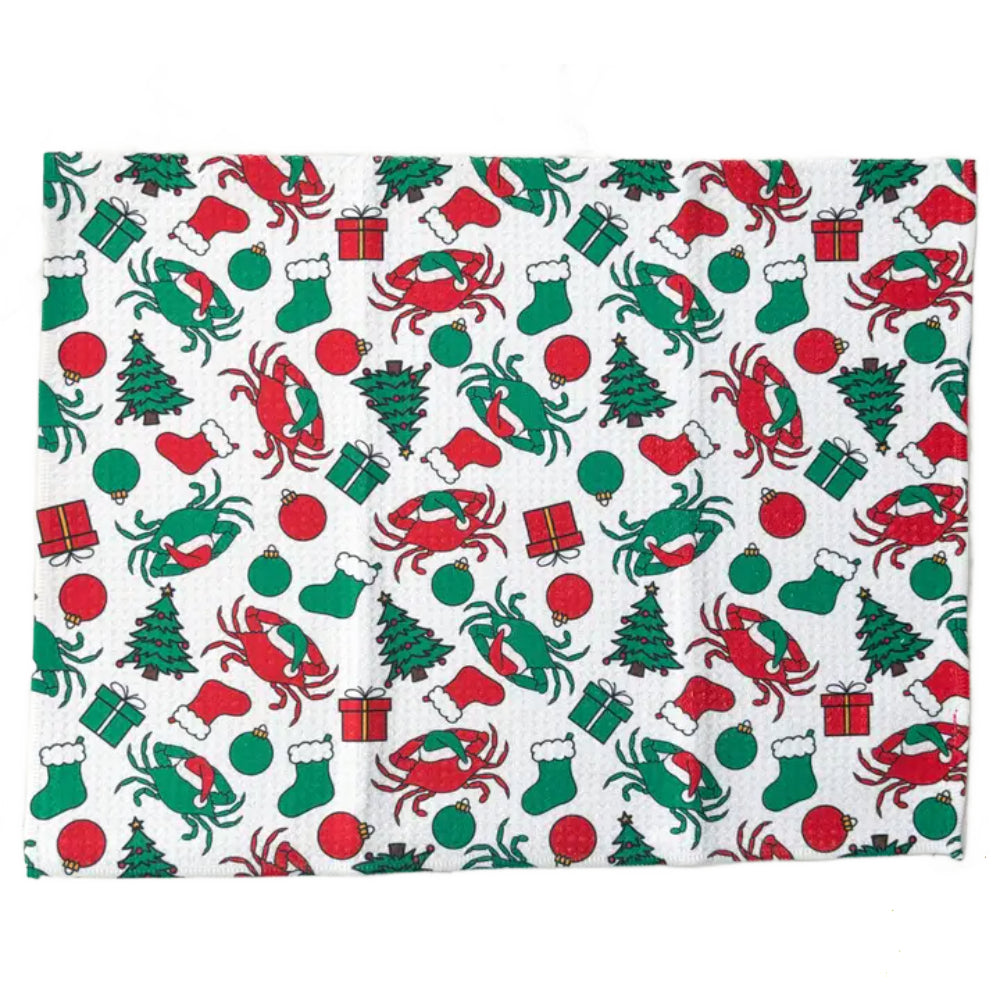 A rectangular white kitchen towel or placemat featuring a festive Christmas pattern with red and green crabs, Christmas trees, stockings, ornaments, and gift boxes.