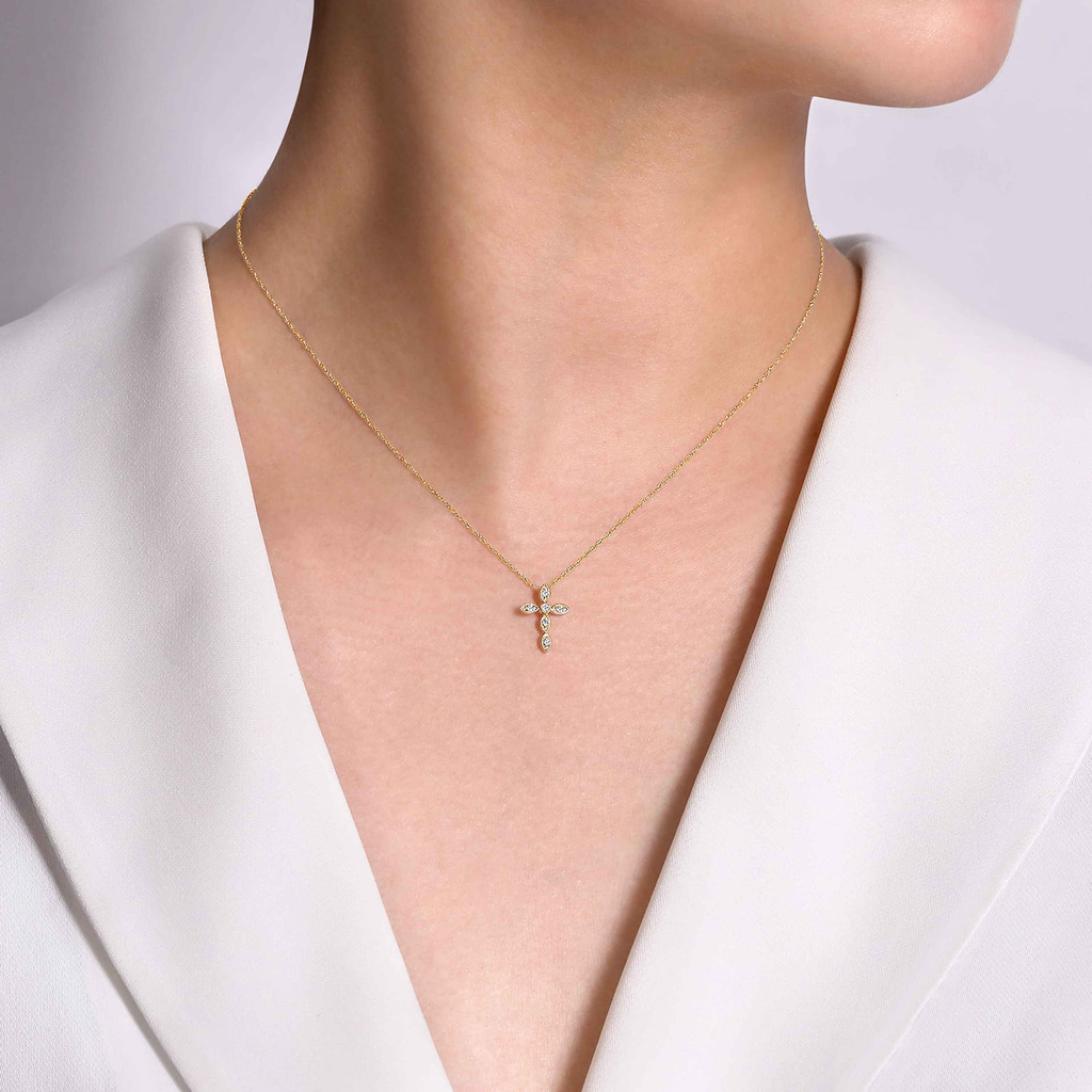 Gold necklace with a cross pendant worn by a person in a white outfit.