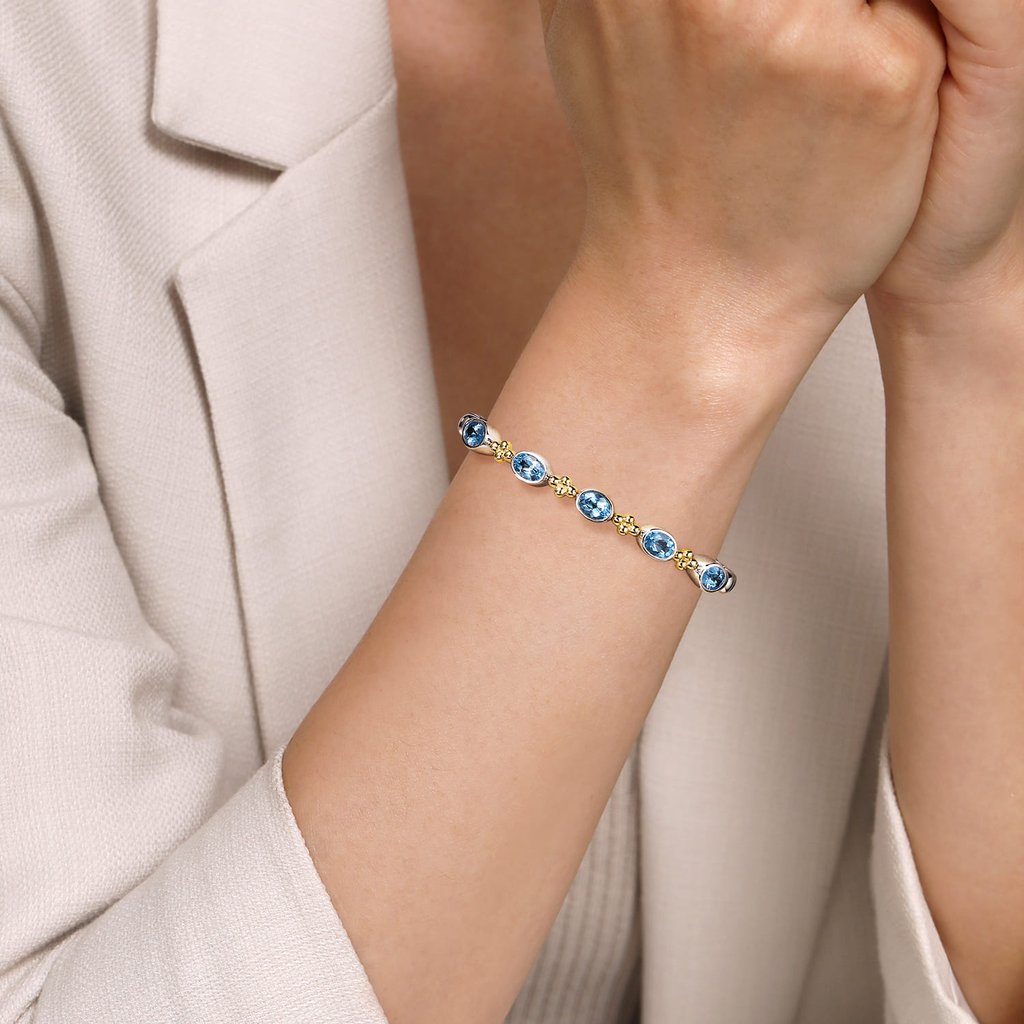Bracelet with blue gemstones on a person's wrist, wearing a light-colored suit.