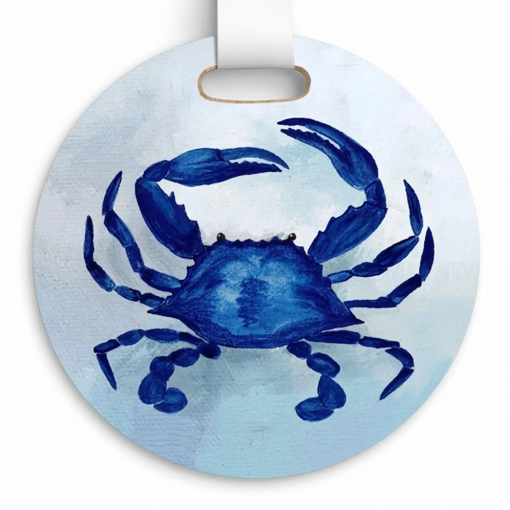 A round white luggage tag featuring a blue watercolor-style crab illustration on a light blue textured background, with a white hanging loop at the top.