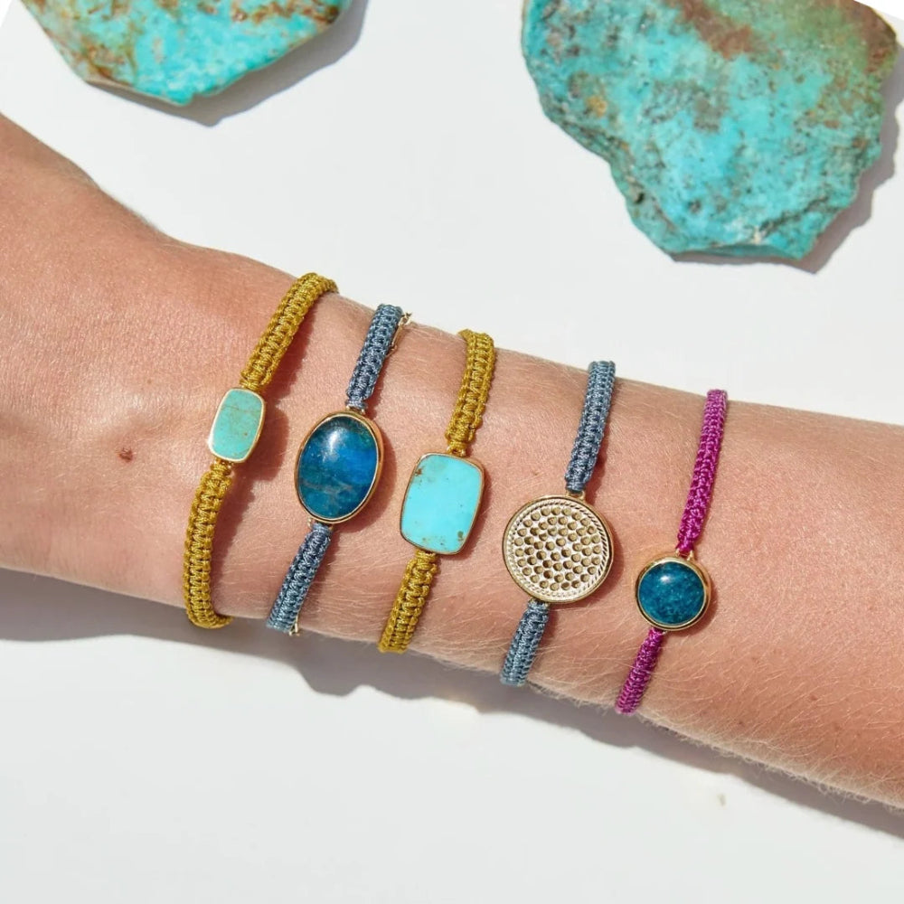 Five colorful woven cord bracelets with various stone and metal accents are displayed on a person's wrist