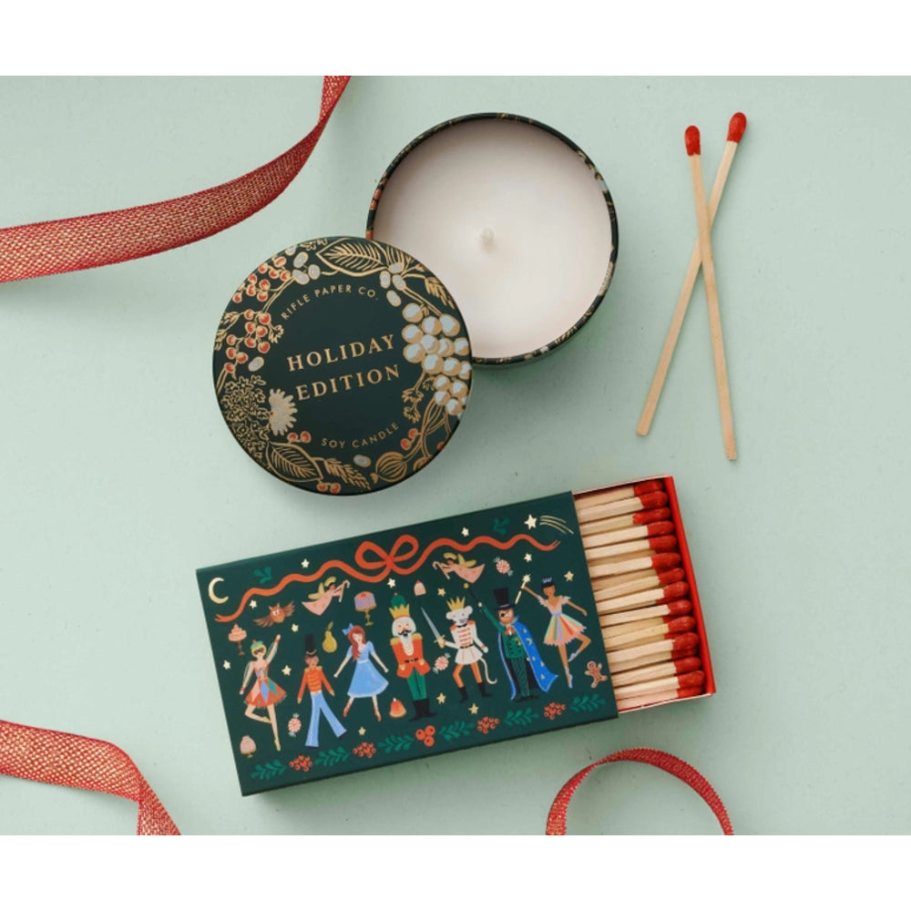 A decorative matchbox of holiday soy candles shown open with several matches beside it, plus the lid and a candle tin on a pale mint background. The matchbox lid reads 'Holiday Edition' and 'Little Paper Co.