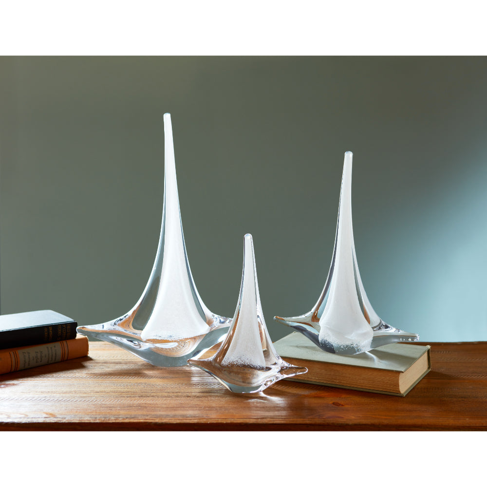 A clear glass sailboat decoration placed on a wooden surface with a neutral background.