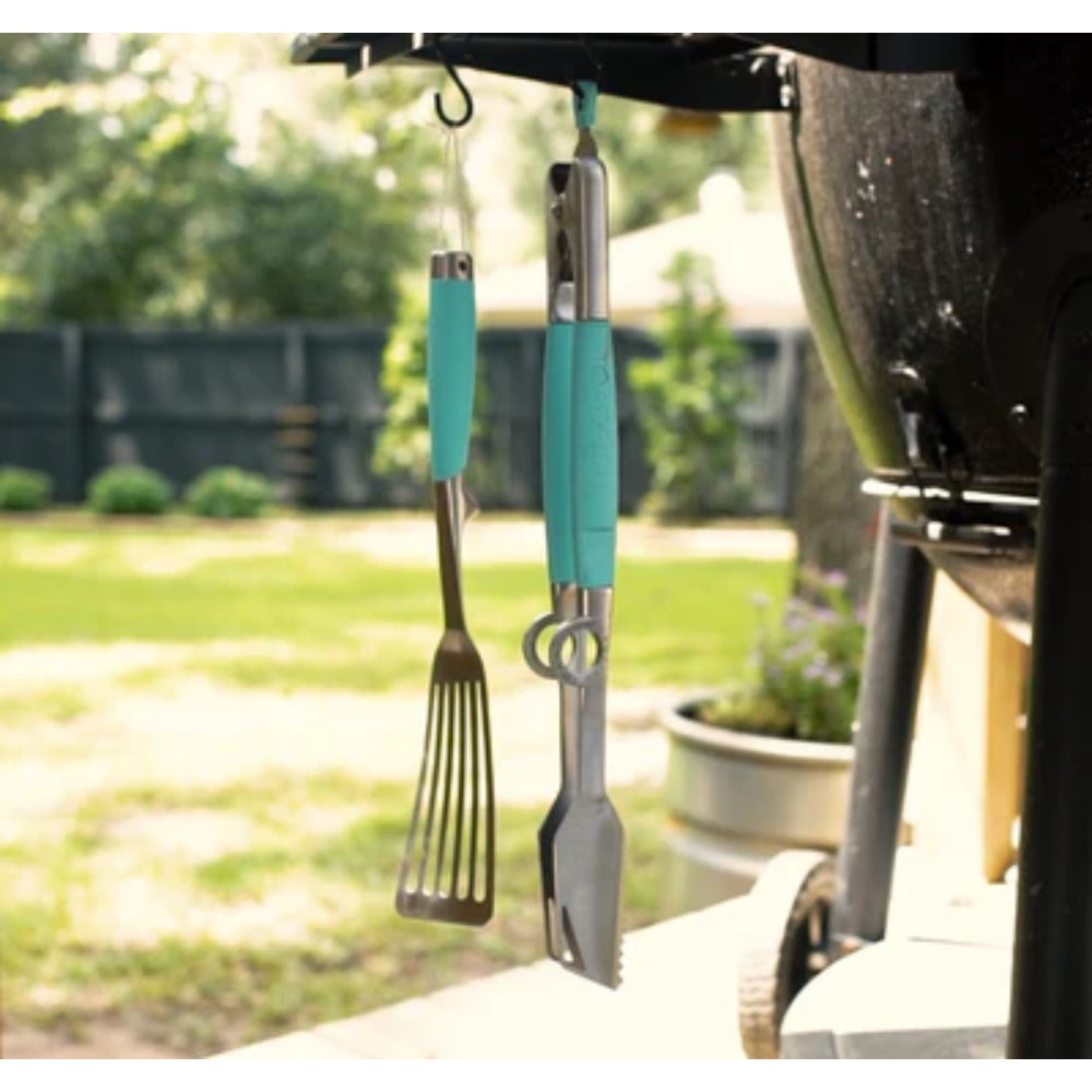 Barbecue tools with turquoise handles hanging from a grill outdoors.