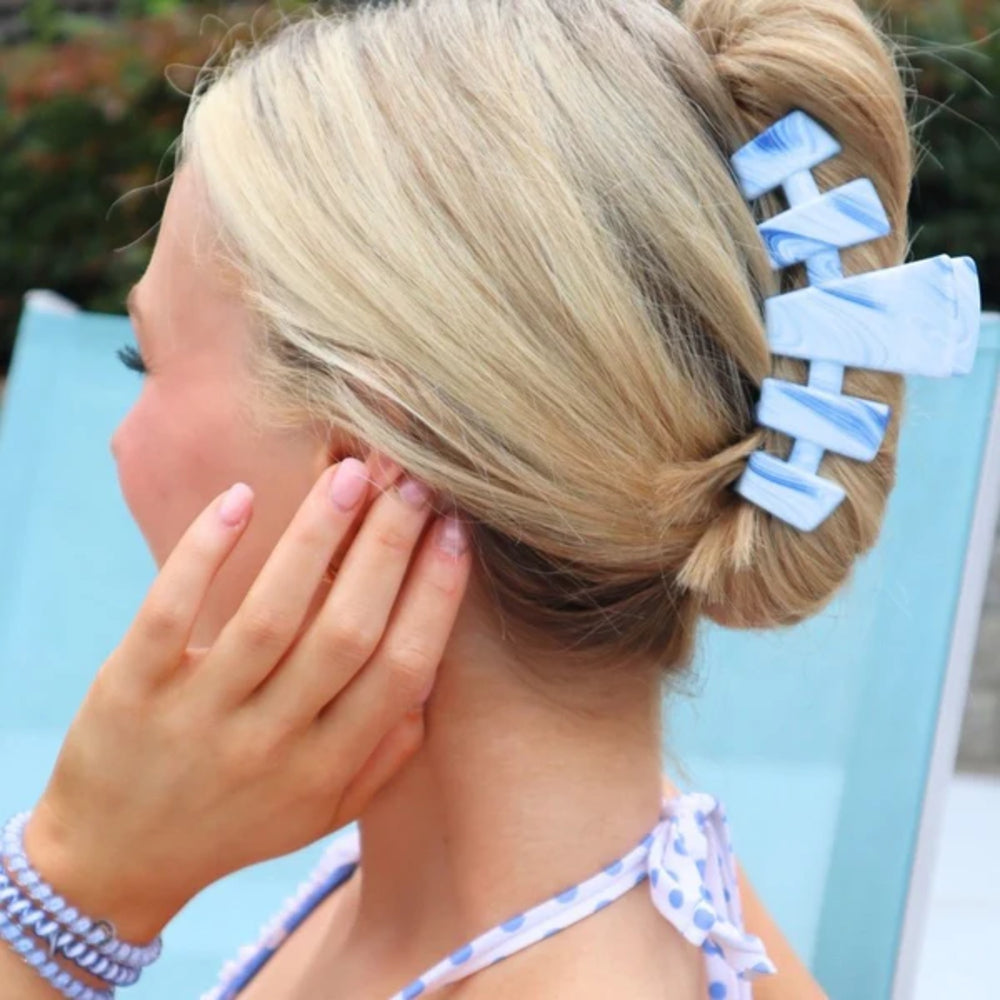 Person with a bun wearing a blue hair clip with letters, sitting on a blue chair.