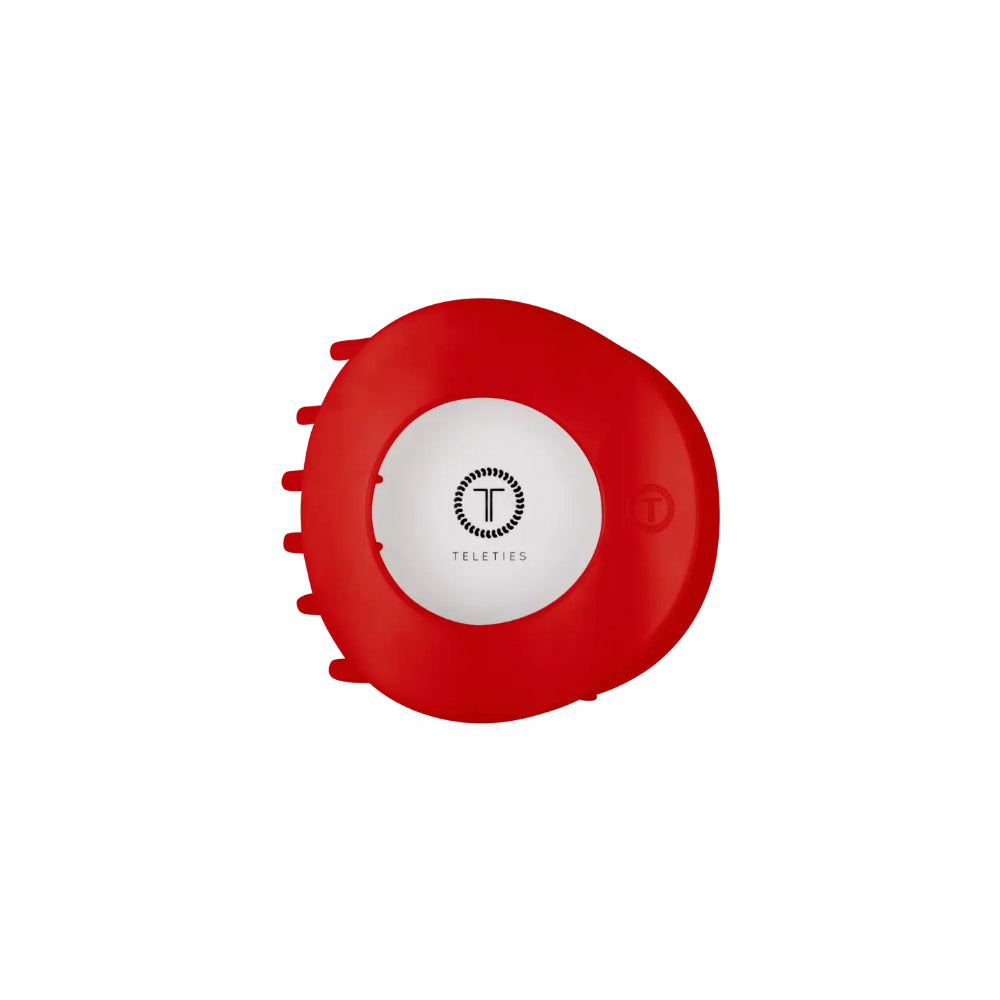 A red circular Teleties hair clip with a white center and black logo, shown on a plain white background.