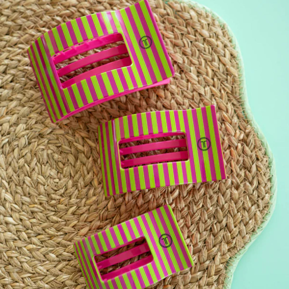 Three pink and green striped boxes on a woven mat with a light blue background