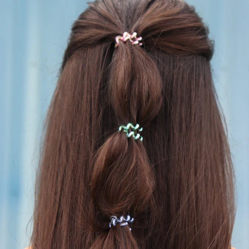 Close-up of a person's hair styled in braids with colorful hair ties against a light blue background