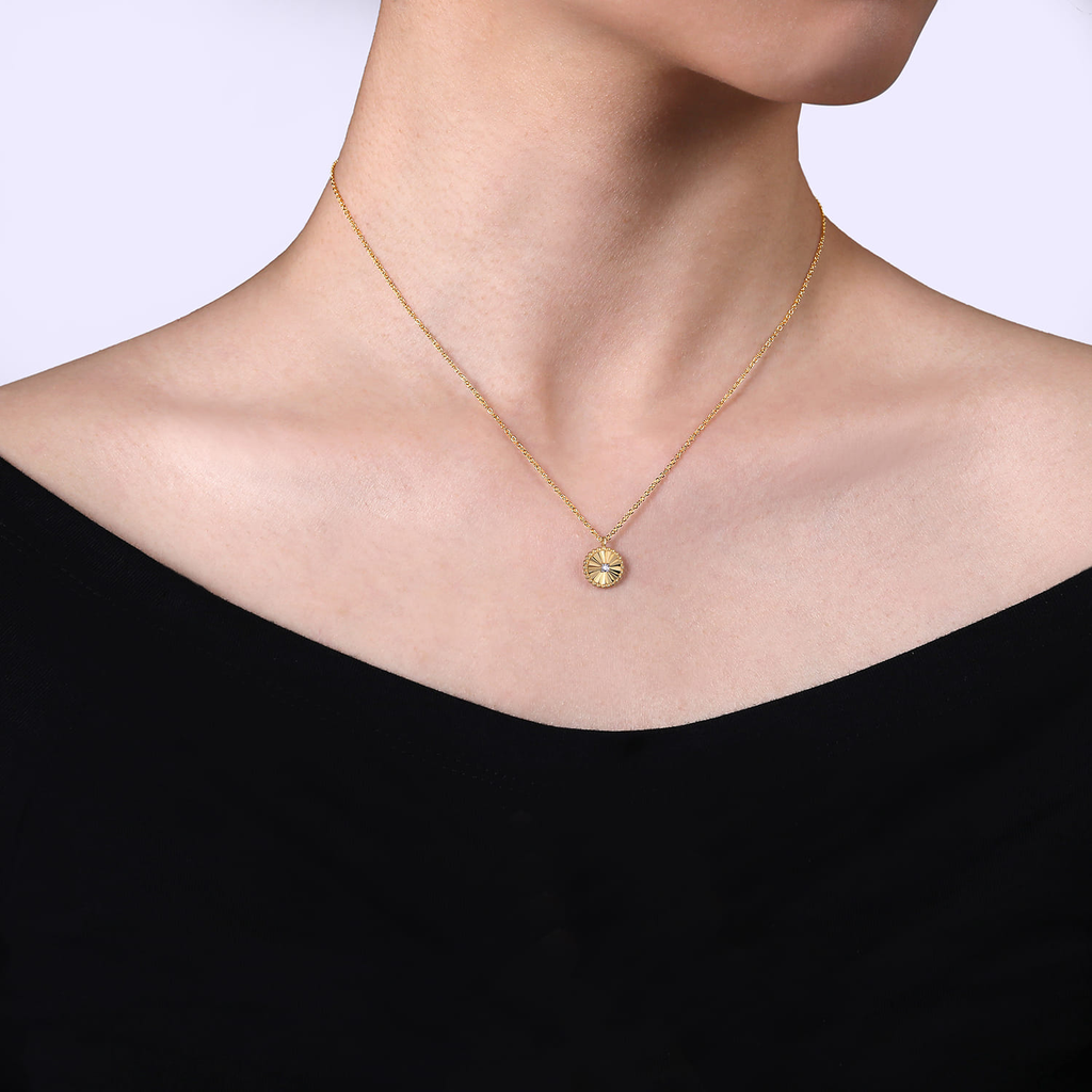 Gold necklace with a small pendant on a person wearing a black top against a white background