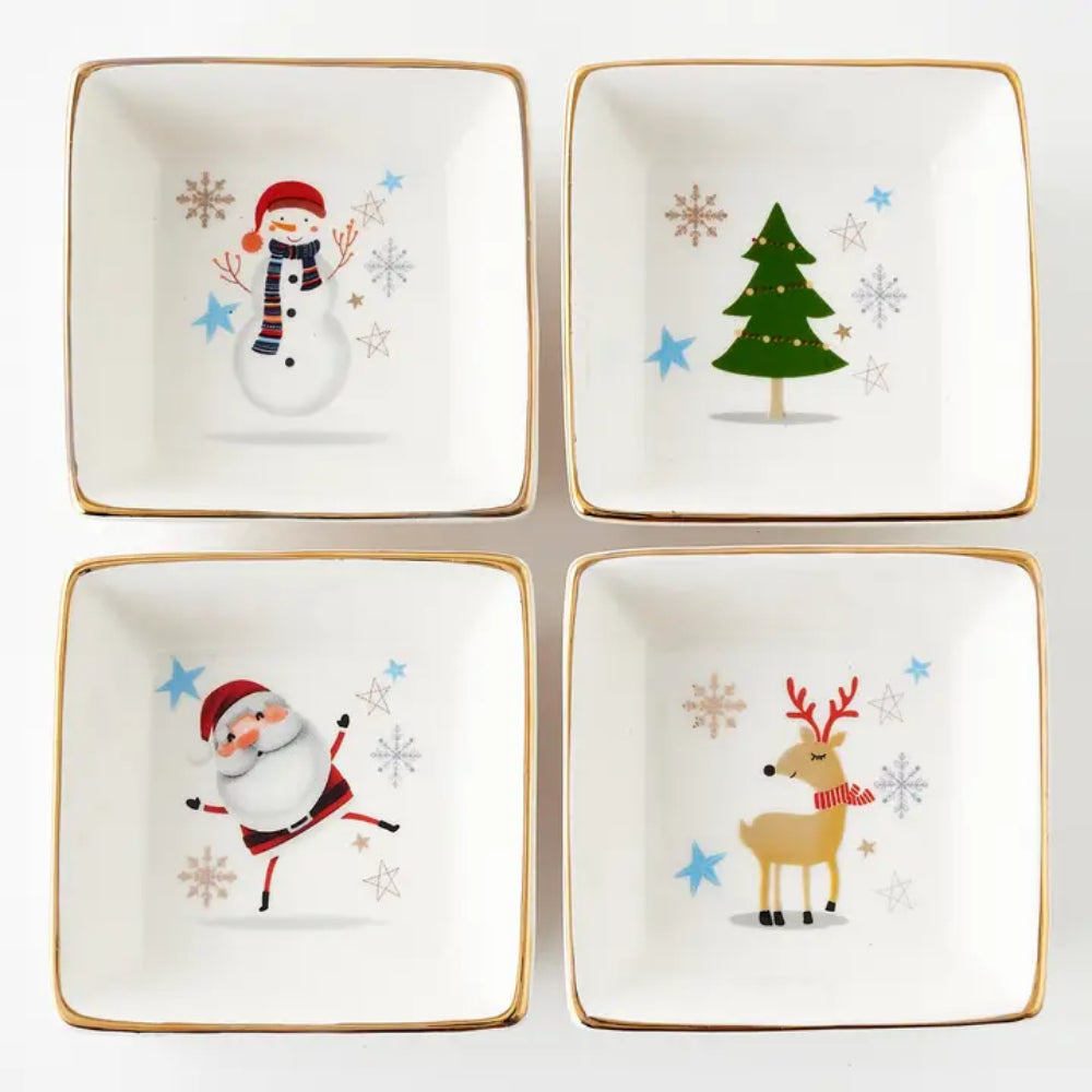 Four square white ceramic dishes with gold trim, arranged in a 2x2 grid. Each dish features a different Christmas illustration: a snowman, a green Christmas tree, Santa Claus, and a reindeer, all on a clean white background.