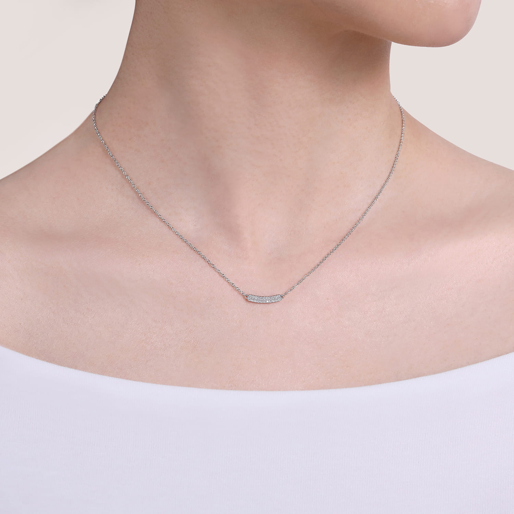 Necklace with a bar pendant worn by a person on a plain background