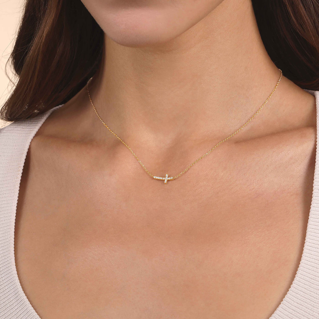 Gold necklace with a small cross pendant on a person wearing a light gray top.