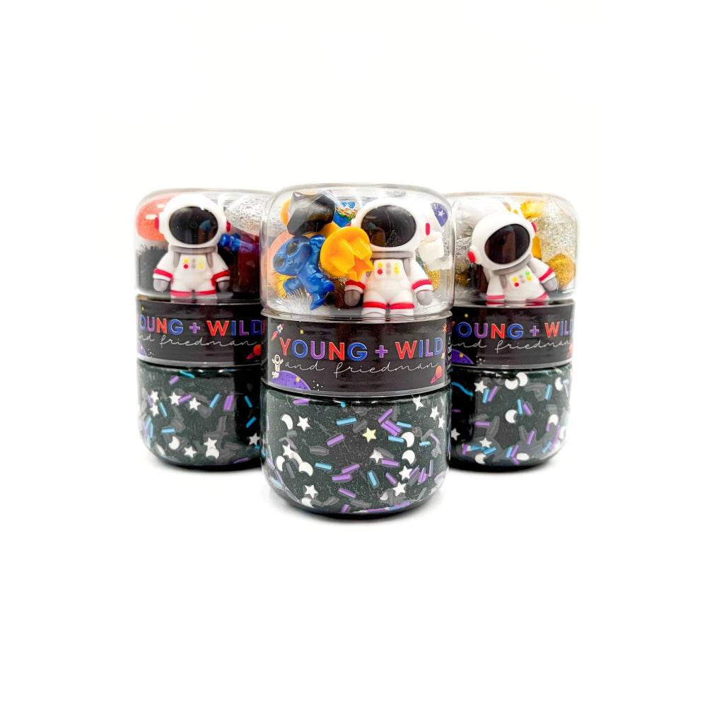 Three small cylindrical containers filled with dark glittery slime and decorated with colorful astronaut figurines, arranged on a plain white background.