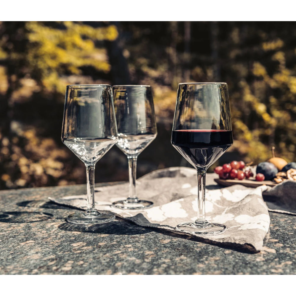 Two empty wine glasses and one filled with red wine on a stone surface with a blurred natural background.