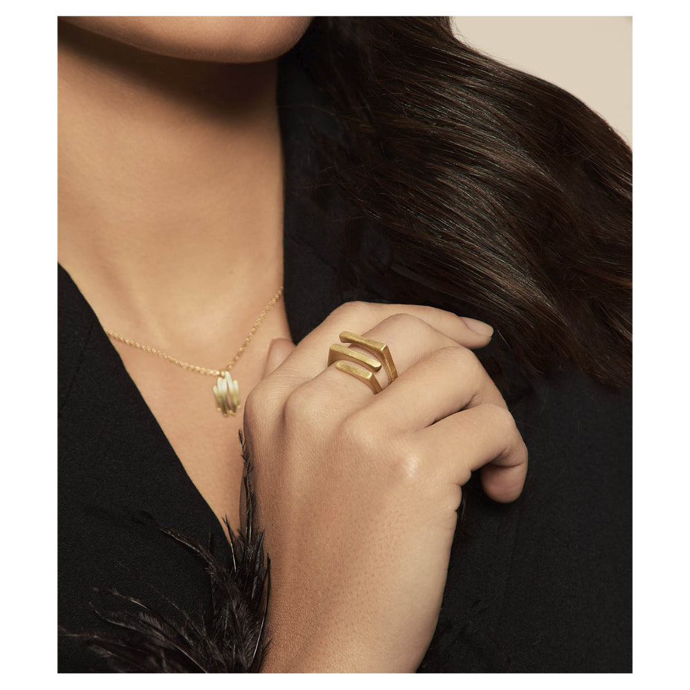 A close-up lifestyle shot of a model wearing a gold geometric ring on her finger, paired with a delicate gold necklace and a black top.