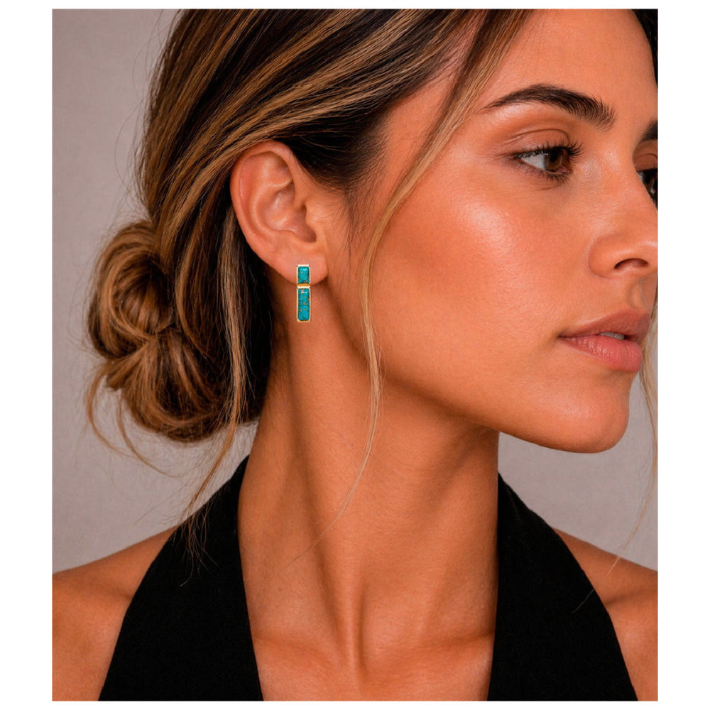 A close-up side profile of a woman wearing a small vertical turquoise earring with a gold-toned setting.
