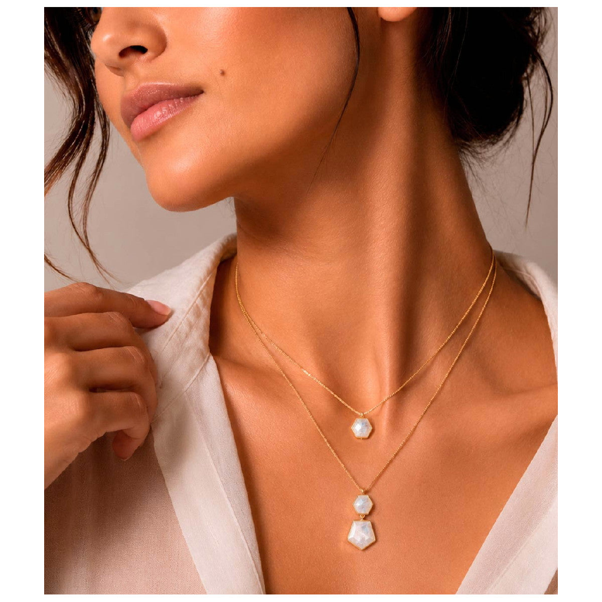 A close-up lifestyle shot of a model wearing a double-layered gold necklace with white pearl-like beads, styled with a white blouse against a neutral background.