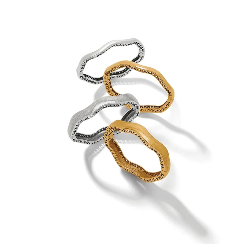 Three abstract wavy bangle in polished yellow gold and silver, arranged diagonally on a clean white background with soft shadows.