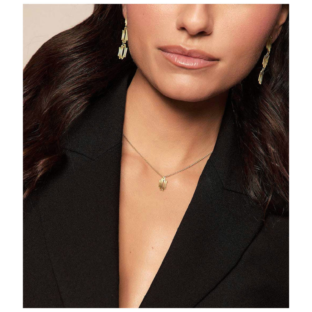 Close-up of a woman wearing a delicate gold leaf pendant necklace and matching gold dangle earrings, styled with a black blazer.