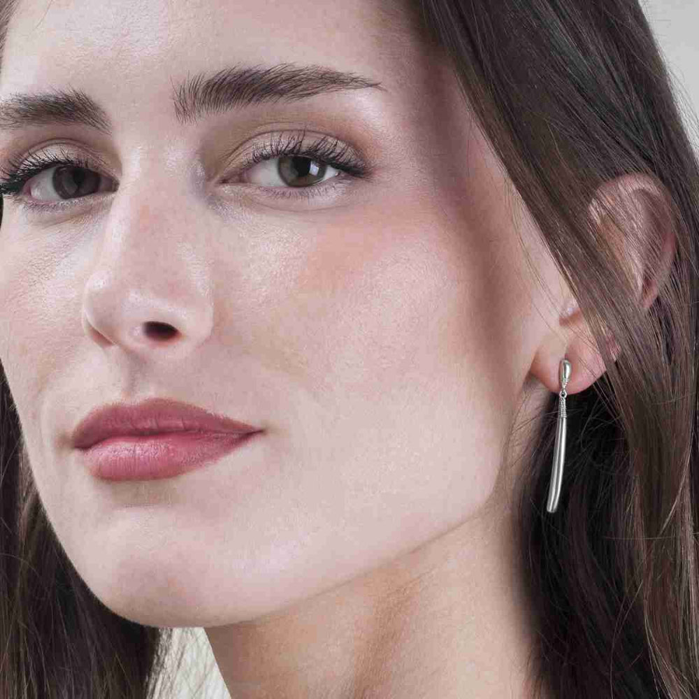 Close-up of a woman wearing a delicate silver drop earring with a thin vertical bar.
