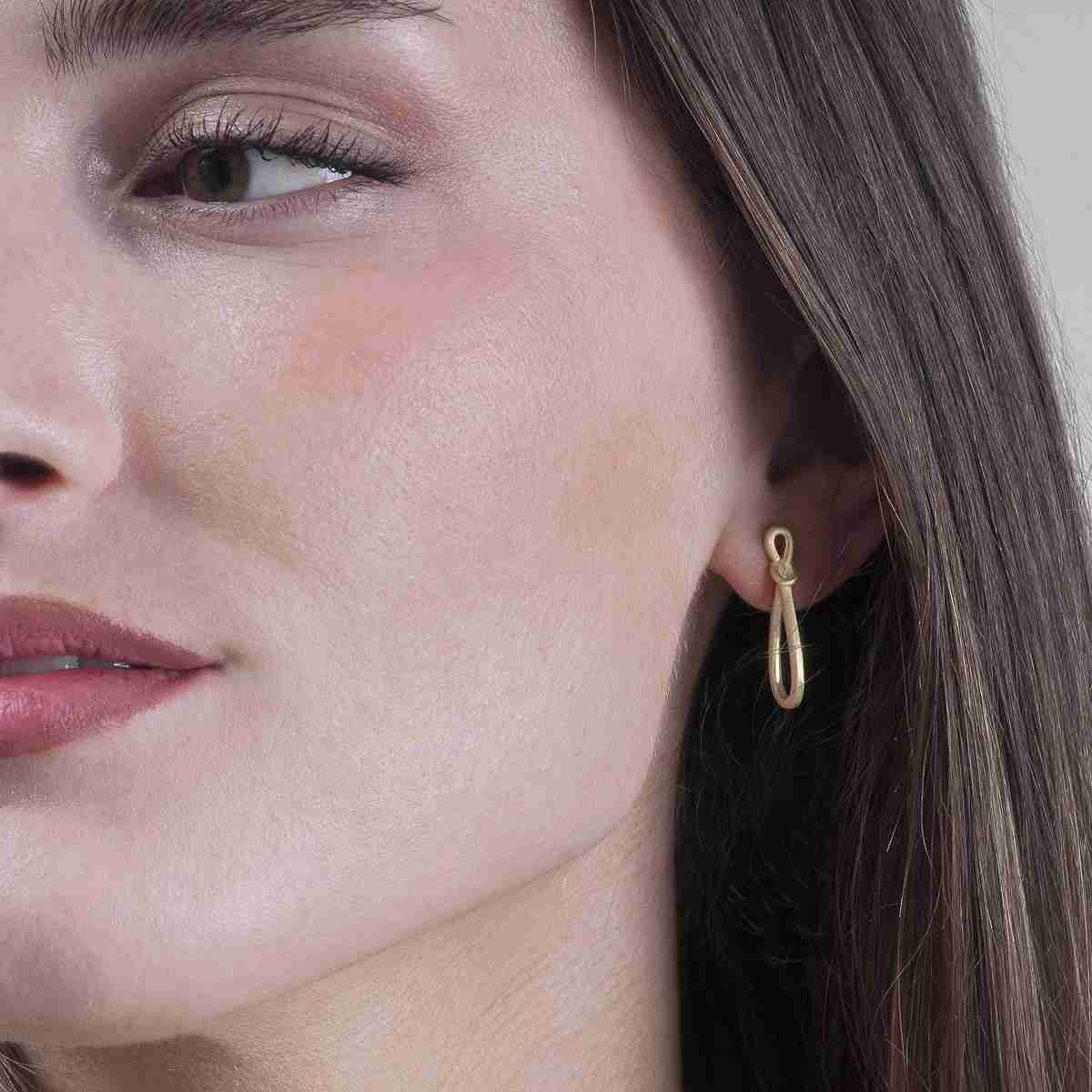 A close-up of a woman's ear wearing a small gold teardrop-shaped hoop earring.