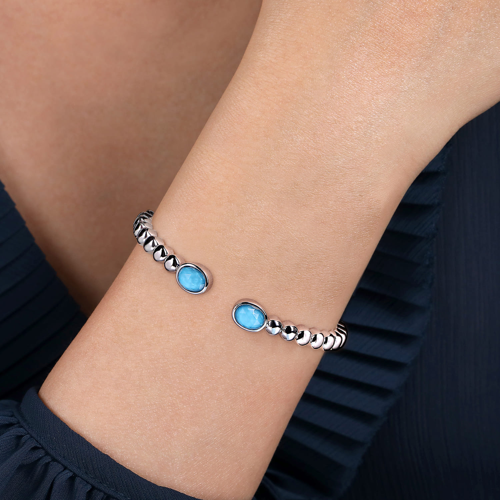 Silver bracelet with blue stones on a wrist against a dark background