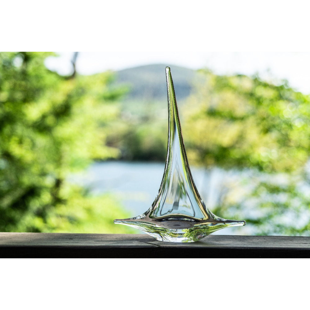 Clear glass sculpture on a wooden surface with a blurred natural outdoor background.