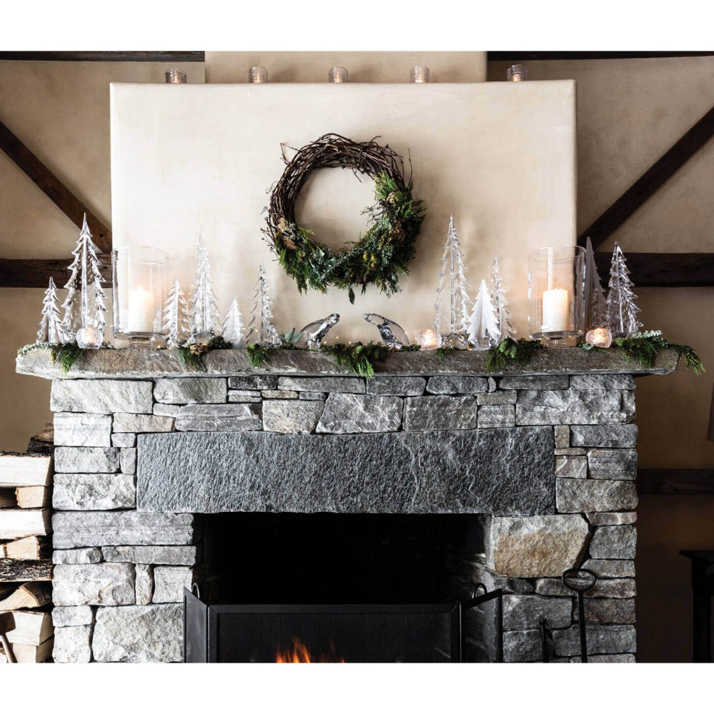 A fireplace with a wreath and Simon Pearce trees in a home display.