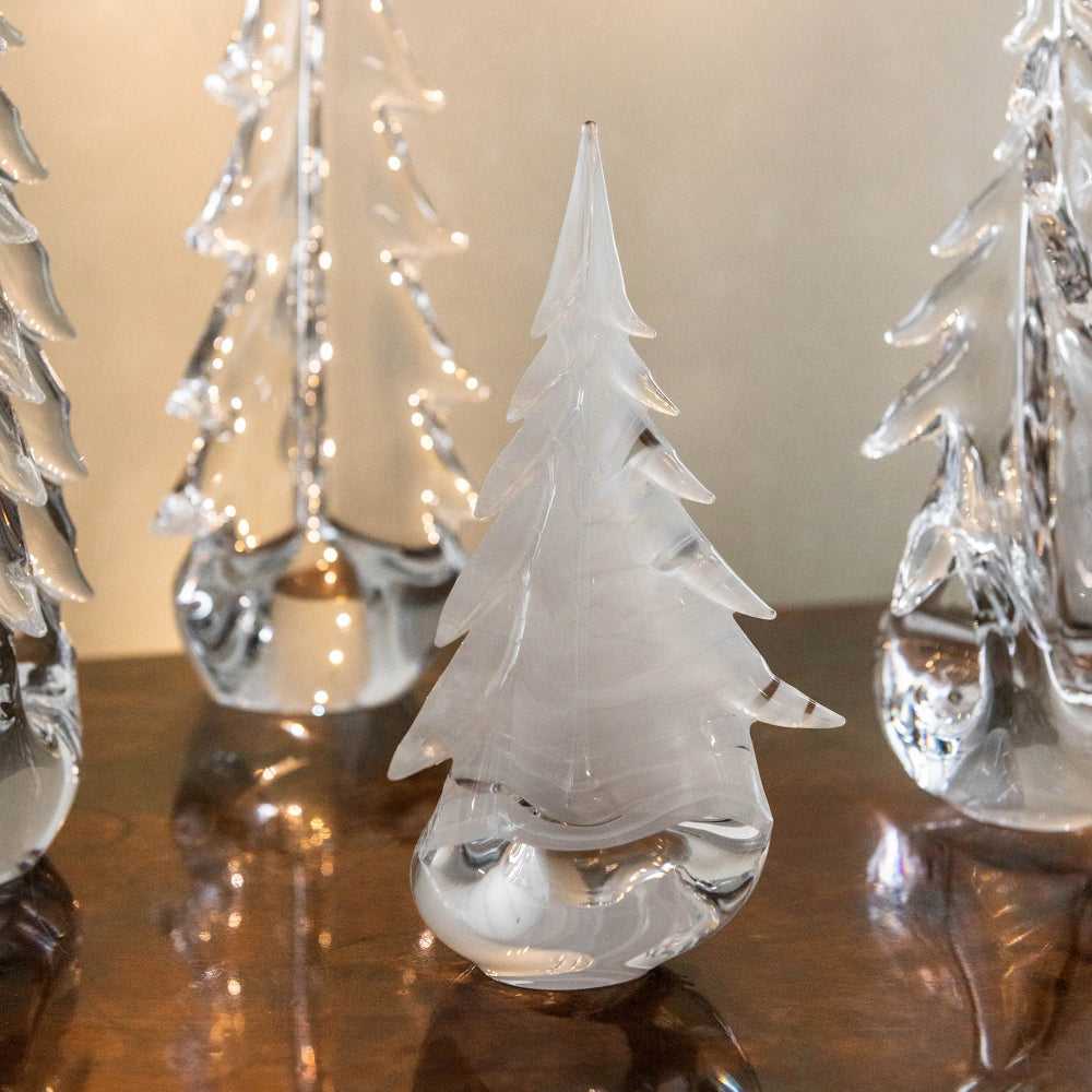 Clear glass Christmas trees on a reflective surface with a neutral background