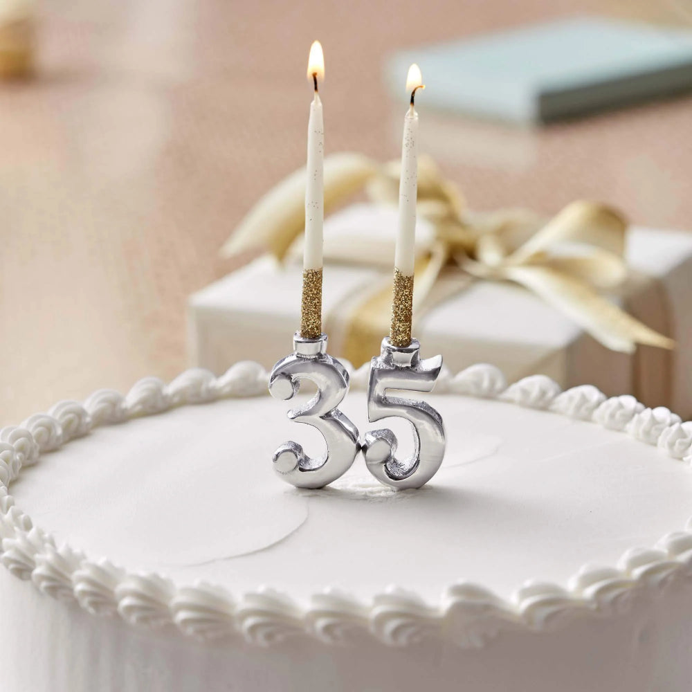 Set of silver metal number cake candles with white candles with the number "35" on a white cake with a blurred backround.