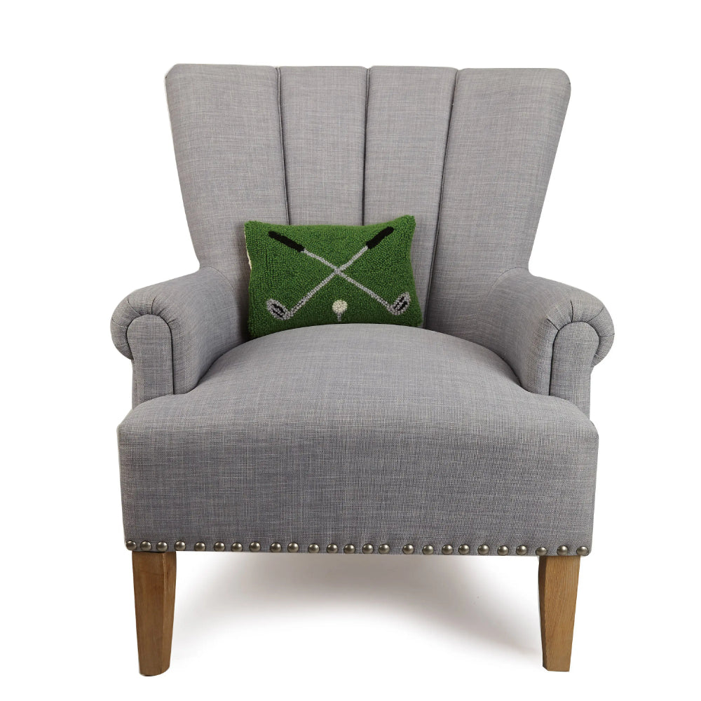 Crossed Golf Clubs Pillow sitting on a grey chair on a white background.