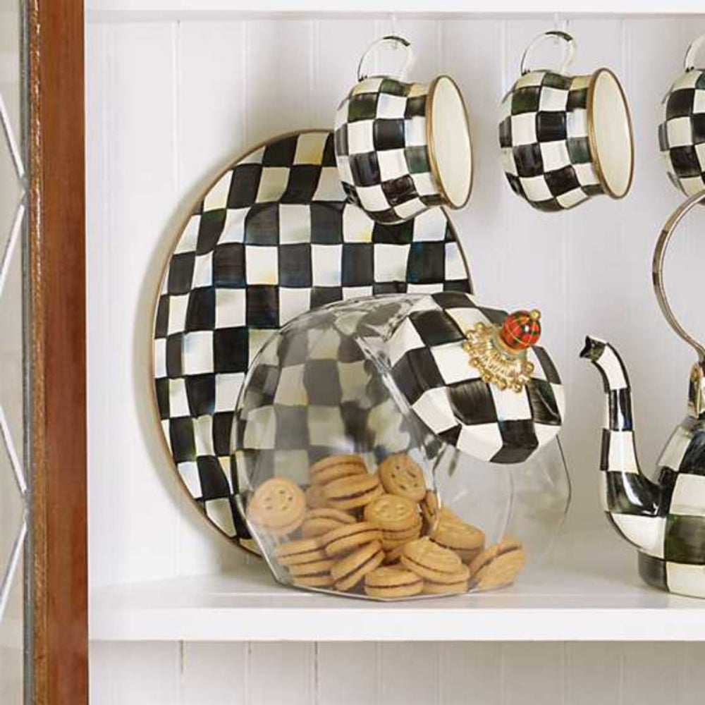 Black and white checkered teapot,plate,cups, and jar with cookies on a shelf.