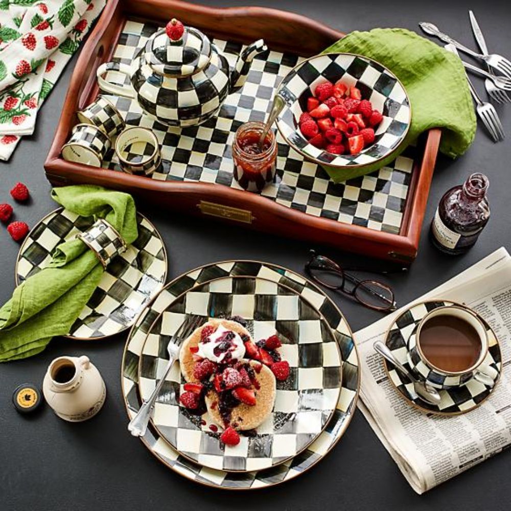 Round plate with black and white with a checkered pattern on a black table with other mackenzie-childs courtly check items