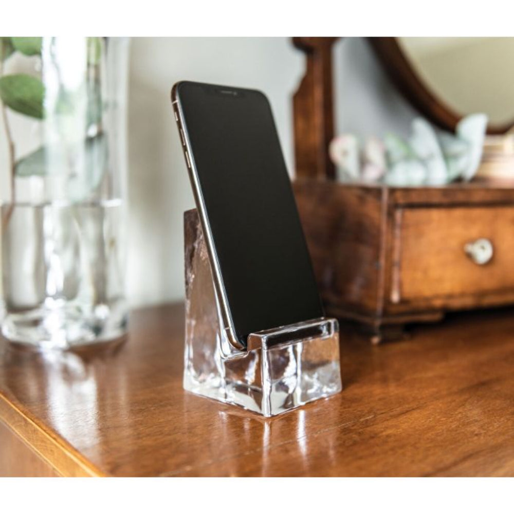 Clear glass phone holder on a brown wood dresser with an Iphone sitting on it