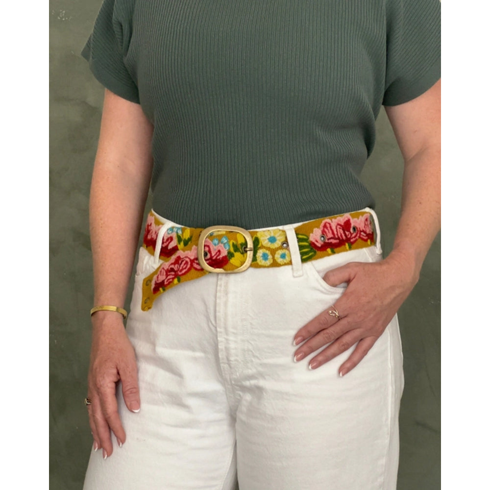 Person wearing a floral belt with a green shirt and white pants on a plain background