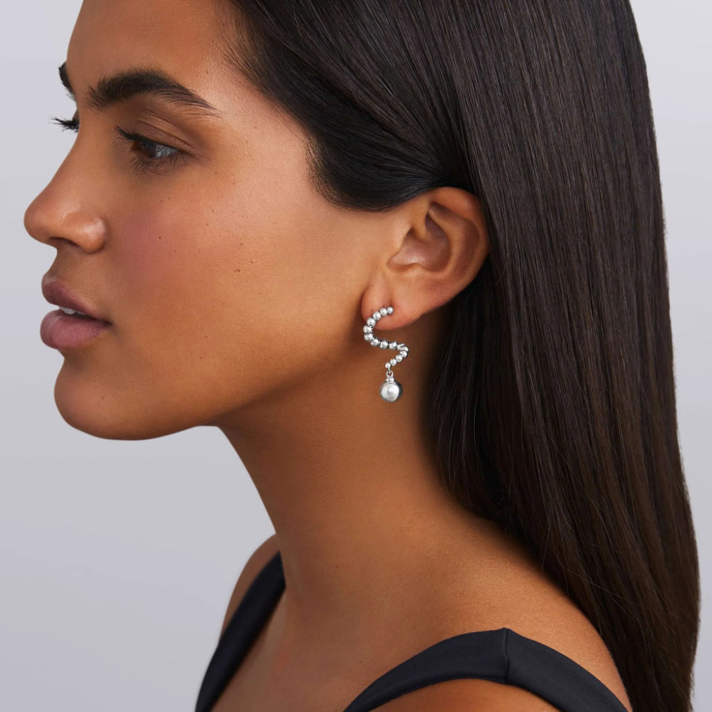 Close-up of a woman wearing a silver earring with a smooth ball at the end of fluid swirl  