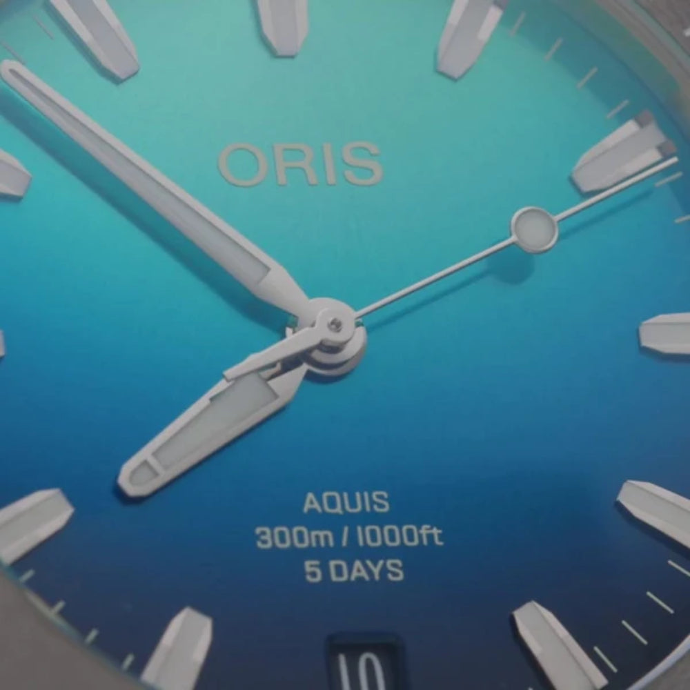 Close-up of an Oris watch face with blue background and white hands.